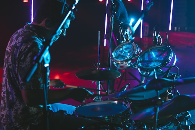 Ein Drummer sitzt lässig an einem Schlagzeug. Ansicht von der Seite. Das Bild ist eine seitliche Aufnahme und insgesamt dunkel und moody. Grund warum Schlagzeug spielen cool ist.